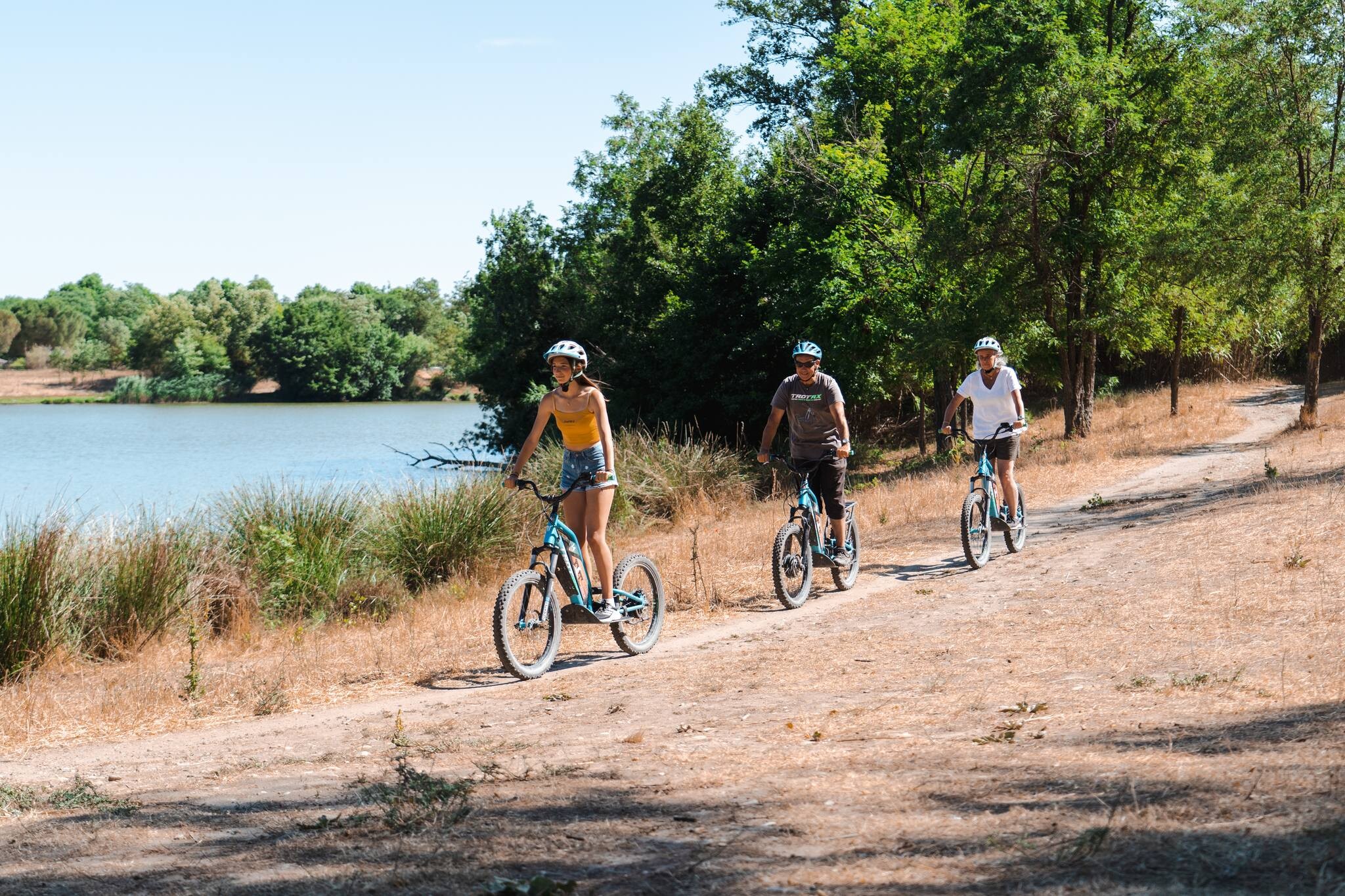 Photo de l'activité scolaire sport nature : le biathlon en trottinette électrique montrant 3 personnes sur des trottinettes en pleine nature, au bord d'un plan d'eau